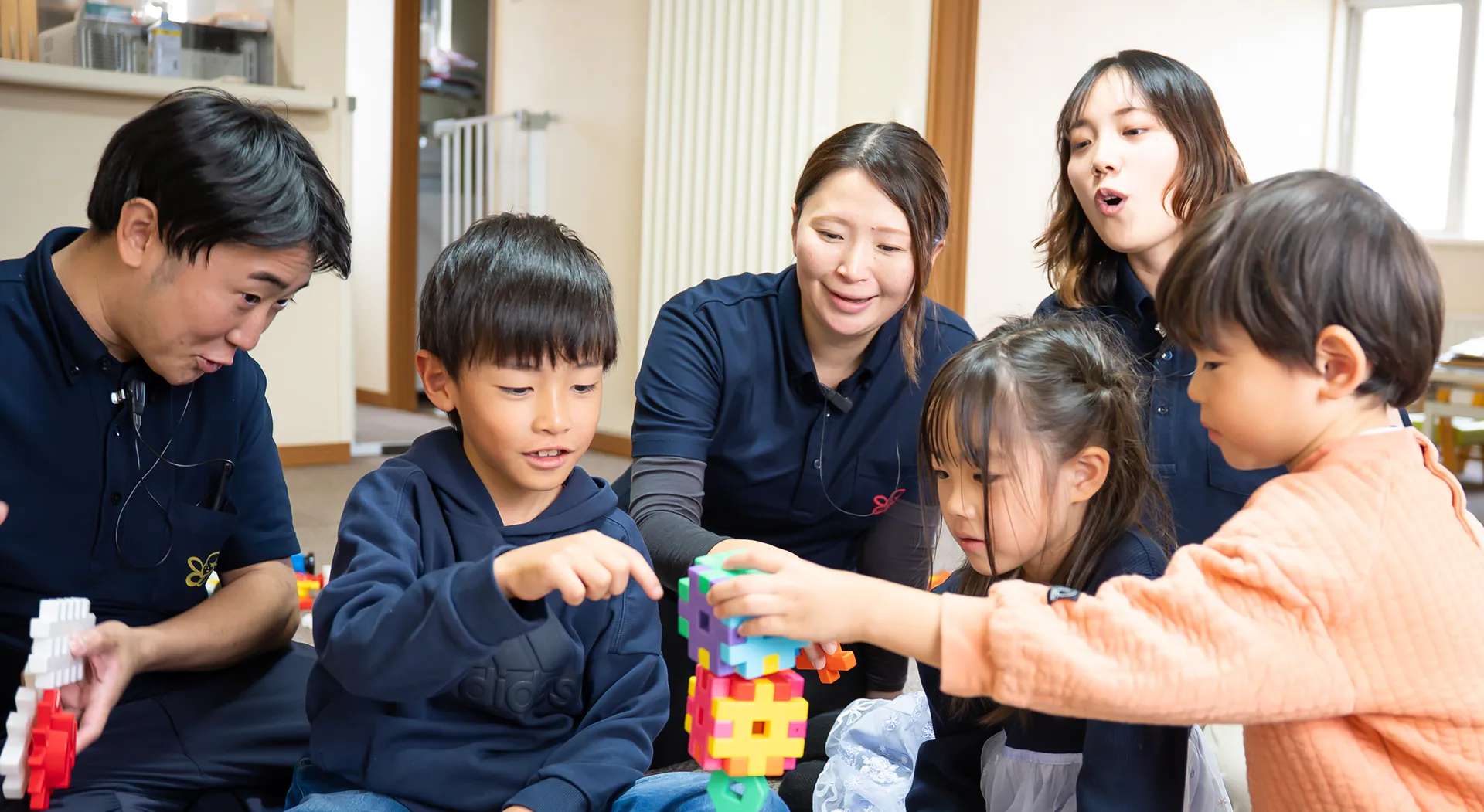 スタッフと子どもたちが一緒にカラフルなブロック遊びを楽しむ様子